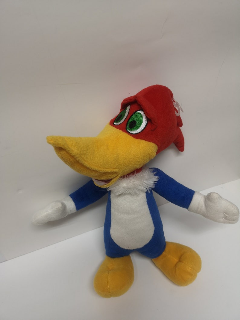 Puede incluir: Un juguete de peluche de Woody Woodpecker, un personaje de dibujos animados. El juguete es rojo, amarillo, azul y blanco. Tiene un sombrero rojo, un pico amarillo, un cuerpo azul y plumas blancas alrededor del cuello.