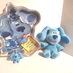 May include: A collection of Blue's Clues themed items. Includes a light blue plush dog, a small figurine, and a cake pan with a Blue's Clues design. The cake pan has a "Happy Birthday Karen" message.
