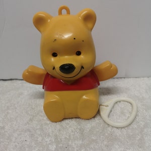May include: A yellow Winnie the Pooh wind-up toy with a red shirt and a white pull string.