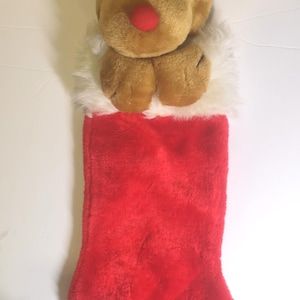 Peut inclure: Une chaussette de Noël en peluche avec une tête de renne au nez rouge et des bois beiges. La chaussette est rouge avec une bordure en fausse fourrure blanche. Décoration de vacances.