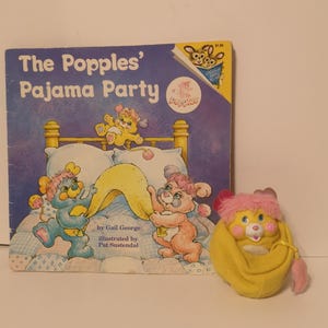 May include: A vintage children's book titled "The Popples' Pajama Party" with illustrations of cartoon characters. Beside the book is a yellow plush Popples toy with pink accents.