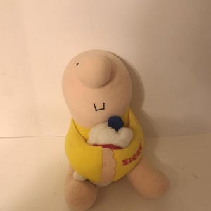 May include: A plush Ziggy doll, featuring a large nose and a yellow shirt. The doll is holding a cupcake with a blue topping. The word "Ziggy" is embroidered on the shirt.