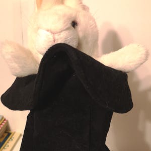 May include: White plush rabbit puppet with black felt hat. The rabbit is peeking out of the hat.