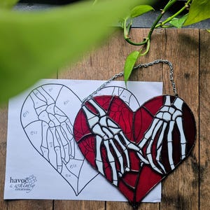 May include: A red and white stained glass heart with skeleton hands holding each other, suspended by a silver chain. A black and white heart diagram is next to the glass heart. The text "havoc & whimsy creations" is on the diagram.