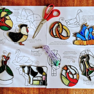 May include: A set of stained glass patterns for crafting projects. The patterns include a rooster, a pear, a swan, a cow, a goose, a ring, a bird, and a heart. The patterns are printed on white paper with black lines and numbers. The patterns are labeled with the text "Havoc & Whimsy Creations".
