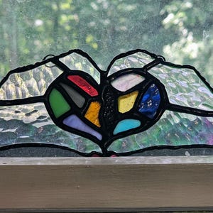 May include: A stained glass heart-shaped window hanging with a variety of colors including red, green, blue, yellow, and purple.