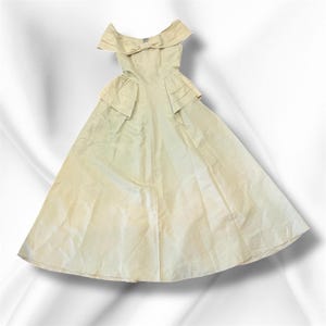 May include: A vintage off-white formal gown with an off-the-shoulder neckline and a full skirt. The bodice features a bow detail and pleated accents. The dress is made of a light, flowing fabric.