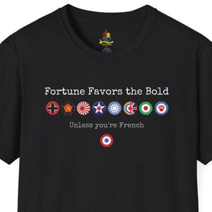 May include: Black t-shirt with the text "Fortune Favors the Bold" and the phrase "Unless you're French." The shirt features a series of colorful circular emblems. A red, white, and blue emblem is at the bottom.