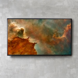 May include: A framed print of a nebula, displaying a palette of orange, teal, and gold hues. The artwork presents a cosmic cloud with star-like specks, set against a grey textured wall. The black frame provides a contemporary contrast to the celestial scene.