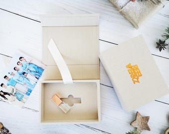 May include: A white box with a gold USB drive inside. The box is open and has a white ribbon tied around it. The box is sitting on a white wooden surface. The box has the text "Reel Very" printed on it.