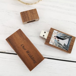 May include: A rectangular wooden USB flash drive with a removable cap. The drive body features a printed photograph of a couple on stairs, while the cap is engraved with the text Our Wedding in a dark font, showcasing a natural wood grain finish.