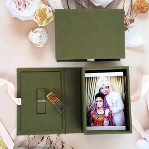 Può includere: Una scatola verde con una foto di una coppia in abiti tradizionali all'interno. La scatola ha uno slot per un'unità USB, che è anche inclusa.