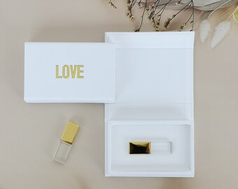 Könnte beinhalten: Eine weiße Box mit einer goldenen Aufschrift "LOVE" und einem transparenten USB-Stick mit goldener Kappe im Inneren.