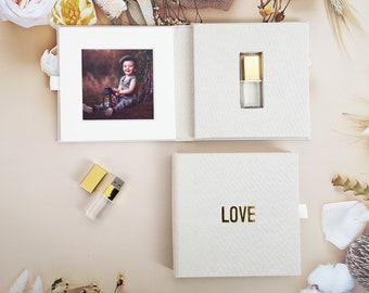 May include: A white linen photo album with a gold USB drive inside. The album has a photo of a child on the front and the word "LOVE" on the back.