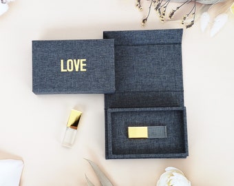 Könnte beinhalten: Eine graue Stoffbox mit dem Wort "LOVE" in goldenen Buchstaben bedruckt. Die Box ist geöffnet und ein goldener und transparenter USB-Stick befindet sich darin.