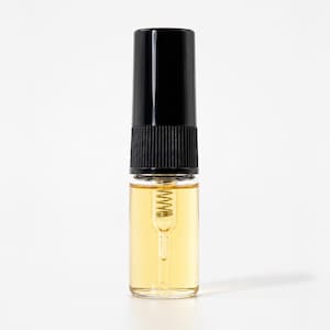 May include: A small, clear glass vial filled with a light amber liquid, featuring a black cylindrical cap with a ribbed base. Inside the vial, a thin, transparent dip tube is visible, containing a small, coiled metal spring mechanism.