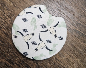 Puede incluir: Posavasos redondo blanco para coche con un patrón de cráneos de toro estilizados verdes y negros y diseños geométricos.