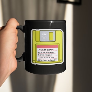 Può includere: Tazza nera con un adesivo di floppy disk giallo che dice "ZERO COOL, LORD NIKON, ACID BURN, THE PHREAK, CEREAL KILLER" in testo rosso.