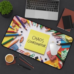 May include: A rectangular desk mat featuring a bright yellow sticky note in the center with the text "CHAOS COORDINATOR" printed in black. The mat is decorated with a colorful pattern of scattered colored pencils, paper clips, and googly eyes.