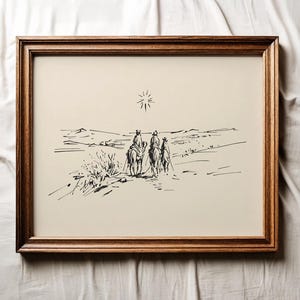 May include: A framed black and white ink drawing depicts three figures on horseback traveling across a desert landscape. A bright star shines above them. The artwork is encased in a dark brown wooden frame.