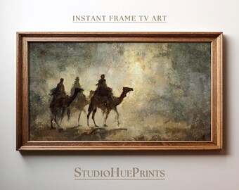 Op de afbeelding: Een ingelijste print met een woestijnscène met drie figuren op kamelen. Het kunstwerk heeft een gedempte kleurenpalet van bruin, beige en grijs. De tekst luidt "INSTANT FRAME TV ART" en "StudioHuePrints".