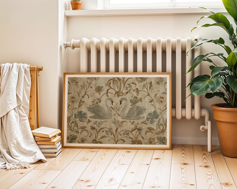May include: A framed artwork featuring two swans amidst floral and foliage patterns in muted tones of beige, blue, and brown. The artwork is displayed on a light wood floor, near a radiator and a potted plant.