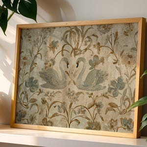 May include: A framed artwork featuring a vintage-style design. The artwork showcases two swans facing each other, surrounded by floral and botanical elements in muted blue, brown, and beige tones. The frame is made of light-colored wood.