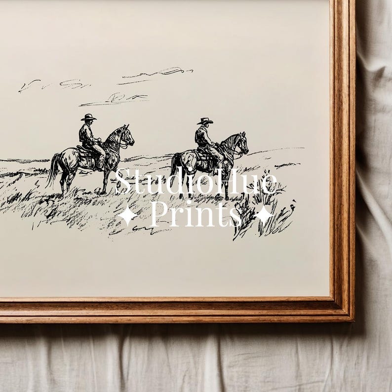 May include: A framed black and white print featuring two cowboys on horseback in a grassy field. The artwork has a vintage aesthetic, with the text "Studio Hue Prints" in the center. The frame is made of wood.