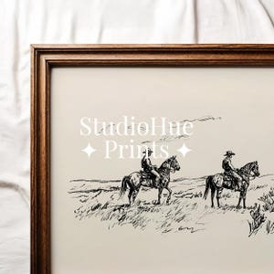 May include: A framed print featuring a black and white sketch of two riders on horseback traversing a grassy landscape. The print has the text "StudioHue Prints" in a decorative font.