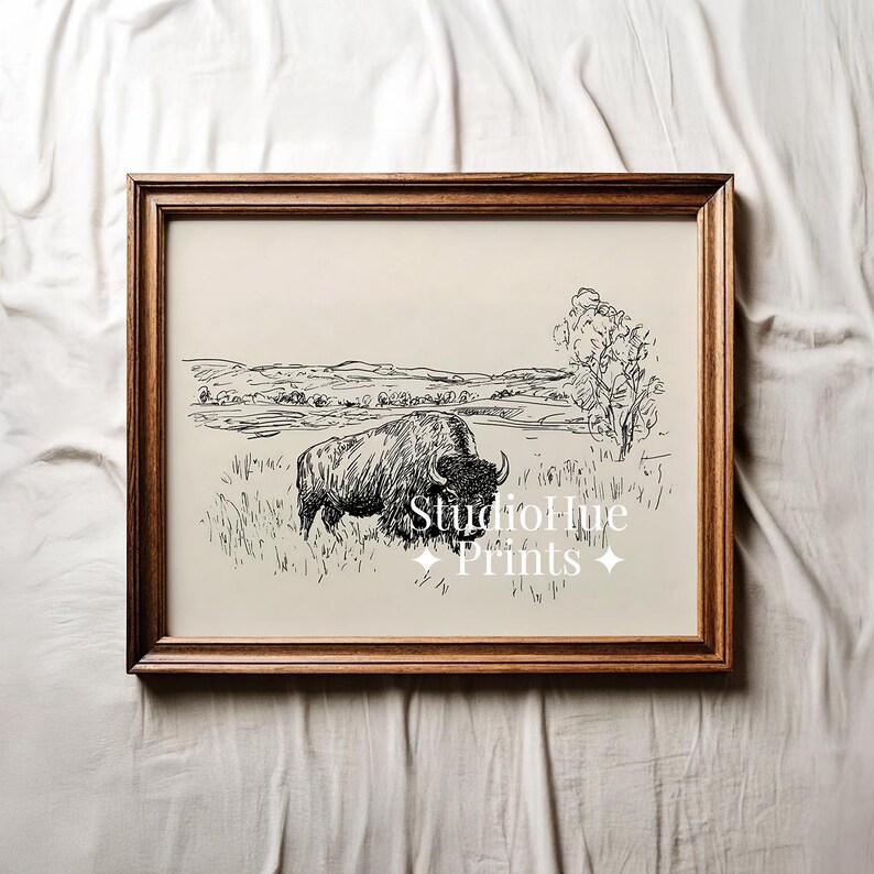 K&ouml;nnte beinhalten: Ein gerahmter Schwarz-Wei&szlig;-Druck eines Bisons auf einem Feld. Das Kunstwerk ist eine Feder- und Tinte-Zeichnung mit einem Landschaftshintergrund. Der Rahmen ist dunkelbraun und der Druck tr&auml;gt den Text "StudioHue Prints".