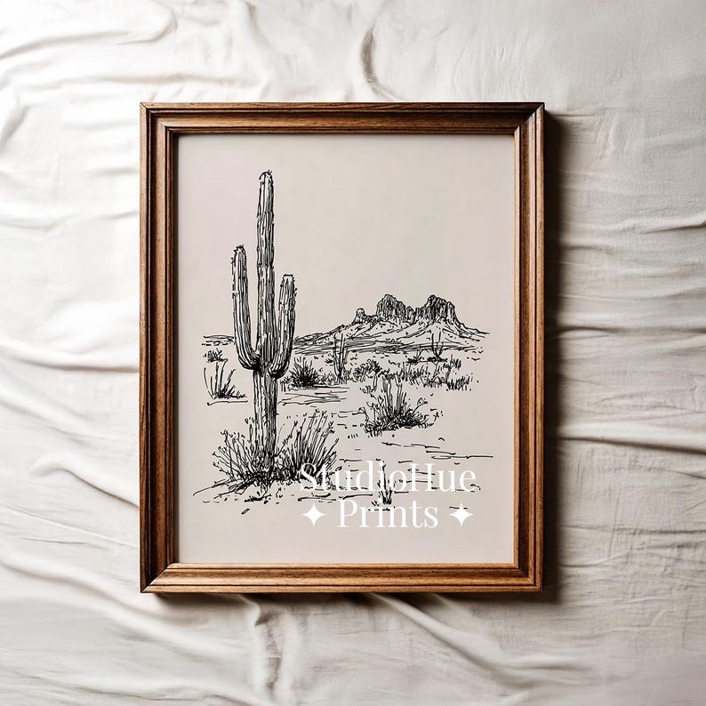 K&ouml;nnte beinhalten: Gerahmter Schwarz-Wei&szlig;-Kunstdruck einer W&uuml;stenlandschaft mit einem Saguaro-Kaktus, Bergen und W&uuml;stenpflanzen. Das Kunstwerk befindet sich in einem Holzrahmen und enth&auml;lt den Text "Studio Hue Prints".