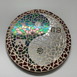 Könnte beinhalten: Runde Mosaikkunst mit Yin-und-Yang-Design. Eine Seite ist irisierend mit Grün-, Blau- und Rosatönen, die andere ist verspiegelt. Der Rand besteht aus einer Mischung aus braunen, roten und goldenen Fliesen. Mit chinesischen Schriftzeichen.