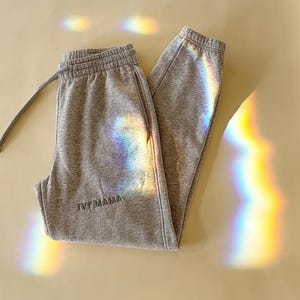Puede incluir: Pantalones de ch&aacute;ndal grises con el texto "IVF Mama" bordado en la pierna izquierda.