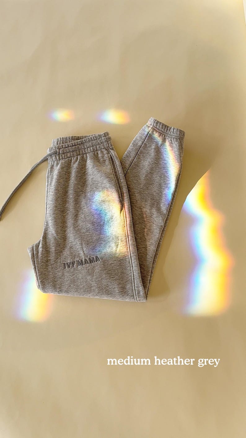 Puede incluir: Pantalones de ch&aacute;ndal grises con el texto "IVF Mama" bordado en la pierna izquierda.