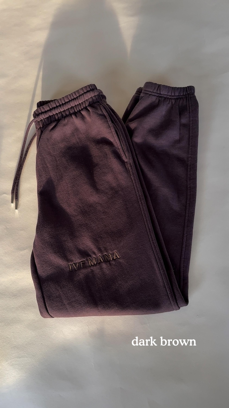 Puede incluir: Pantalones de ch&aacute;ndal de color marr&oacute;n oscuro con cintura el&aacute;stica y el texto "IVF MAMA" bordado en la pierna izquierda.