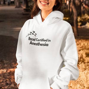 May include: White hoodie with a black graphic that says "...zzz Bored Certified in Anesthesia".