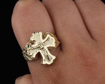 May include: Gold-colored ring featuring a cross design with a figure of Jesus Christ. The ring is worn on a finger, showcasing the intricate details of the religious symbol. The ring has a textured band.