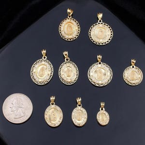 May include: A collection of gold-colored religious pendants in various sizes and designs, including oval and circular shapes. Some pendants feature intricate detailing and are adorned with small, sparkling embellishments. A U.S. quarter is included for size comparison.