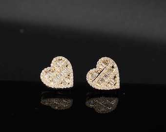 May include: A pair of heart-shaped stud earrings. The earrings are gold-toned and encrusted with small, sparkling, rectangular-cut gemstones. The gemstones are arranged in a diagonal pattern across the heart shape.