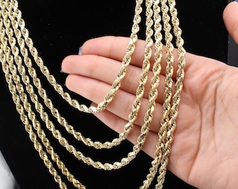 May include: A collection of gold-colored rope chain necklaces. The necklaces are displayed against a black background. The chains are held by a hand, showcasing the texture and design of the jewelry.