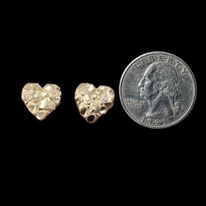 May include: Two gold heart-shaped earrings with a textured surface. The earrings are shown next to a US quarter for size comparison.