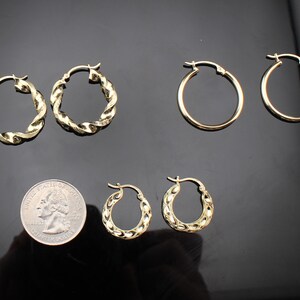 May include: A collection of gold-colored hoop earrings in various styles. The earrings include classic round hoops and textured, twisted designs. A quarter coin is included for size reference, showcasing the different sizes available.