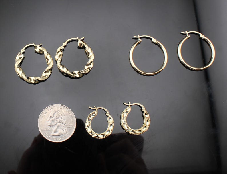 May include: A collection of gold-colored hoop earrings in various styles. The earrings include classic round hoops and textured, twisted designs. A quarter coin is included for size reference, showcasing the different sizes available.