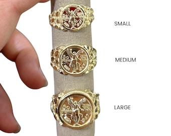 May include: Three gold-colored rings with coin-like centerpieces, displayed on a gray ring holder. The rings are labeled "SMALL", "MEDIUM", and "LARGE". Each ring features a detailed design and a textured band.