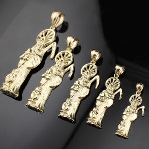 May include: Five gold-colored pendants featuring a religious figure with a halo and a curved staff. The pendants vary in size, with intricate details in the design. The background is a dark, reflective surface.