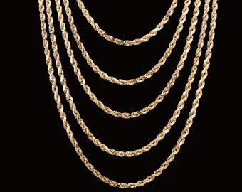 May include: Gold-colored rope chains of varying lengths hang against a black background. The chains are twisted, creating a textured surface. The image showcases a collection of necklaces, highlighting their design and color.