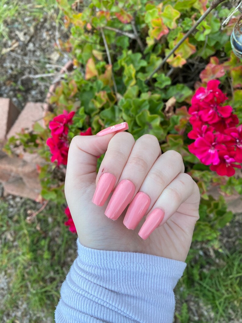 Op de afbeelding: Een hand met lange, lichtroze, amandelvormige nagels. De nagels zijn gelakt in een lichtroze kleur.