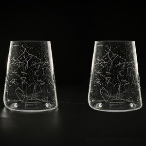 Peut inclure: Deux verres à boire en verre transparent avec un motif de constellation gravé sur le côté. Les verres sont sur une surface noire.