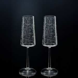 Op de afbeelding: Twee heldere glazen champagneflutes met een gegraveerd sterrenbeeldpatroon in het glas.