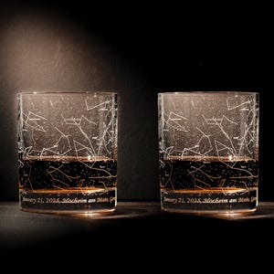 May include: Two clear glass tumblers with a constellation design etched into the glass. The glasses are filled with a dark liquid and have the text "January 21, 2025, Hochheim am Main, G" etched on the bottom.